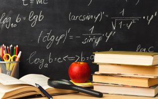 Studying mathematics educational background. Books pile, pencils, scissors, magnifying glass and apple against classroom blackboard with chalk writing of sums. Back to school, research concept